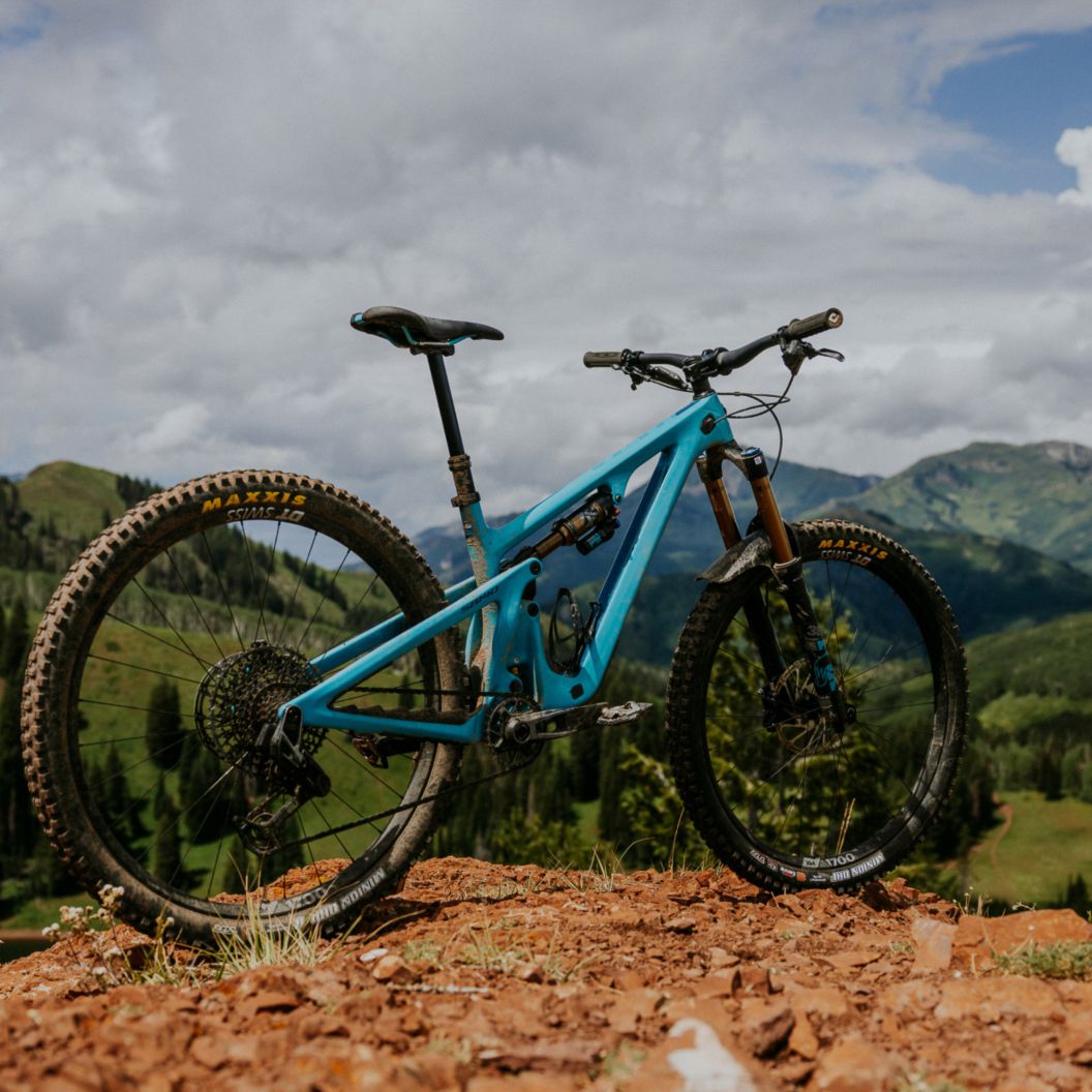 The Yeti SB140 stands in profile overlooking grassy mountains with dispersed trees.